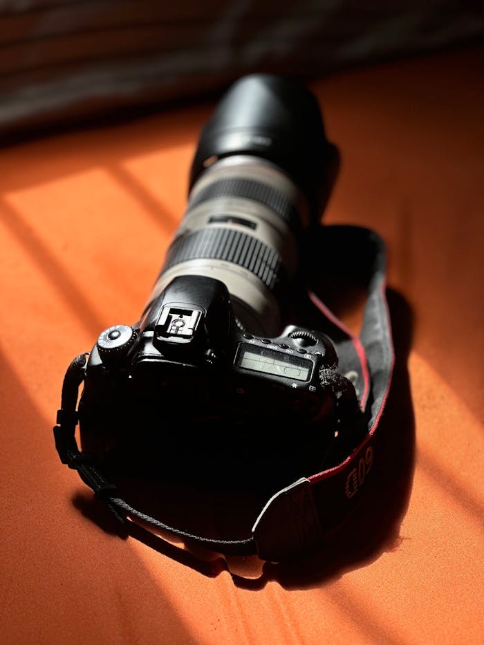 Close-up of a DSLR camera with a telephoto lens on an orange table lit by natural sunlight.